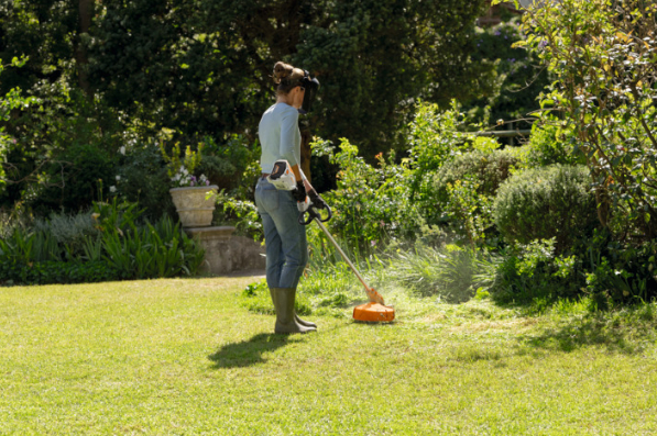 μια γυναίκα περιποιείται το γκαζόν του κήπου της με την μηχανή